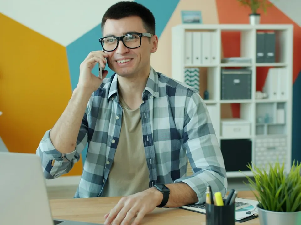 A smiling man on a phone call at his desk